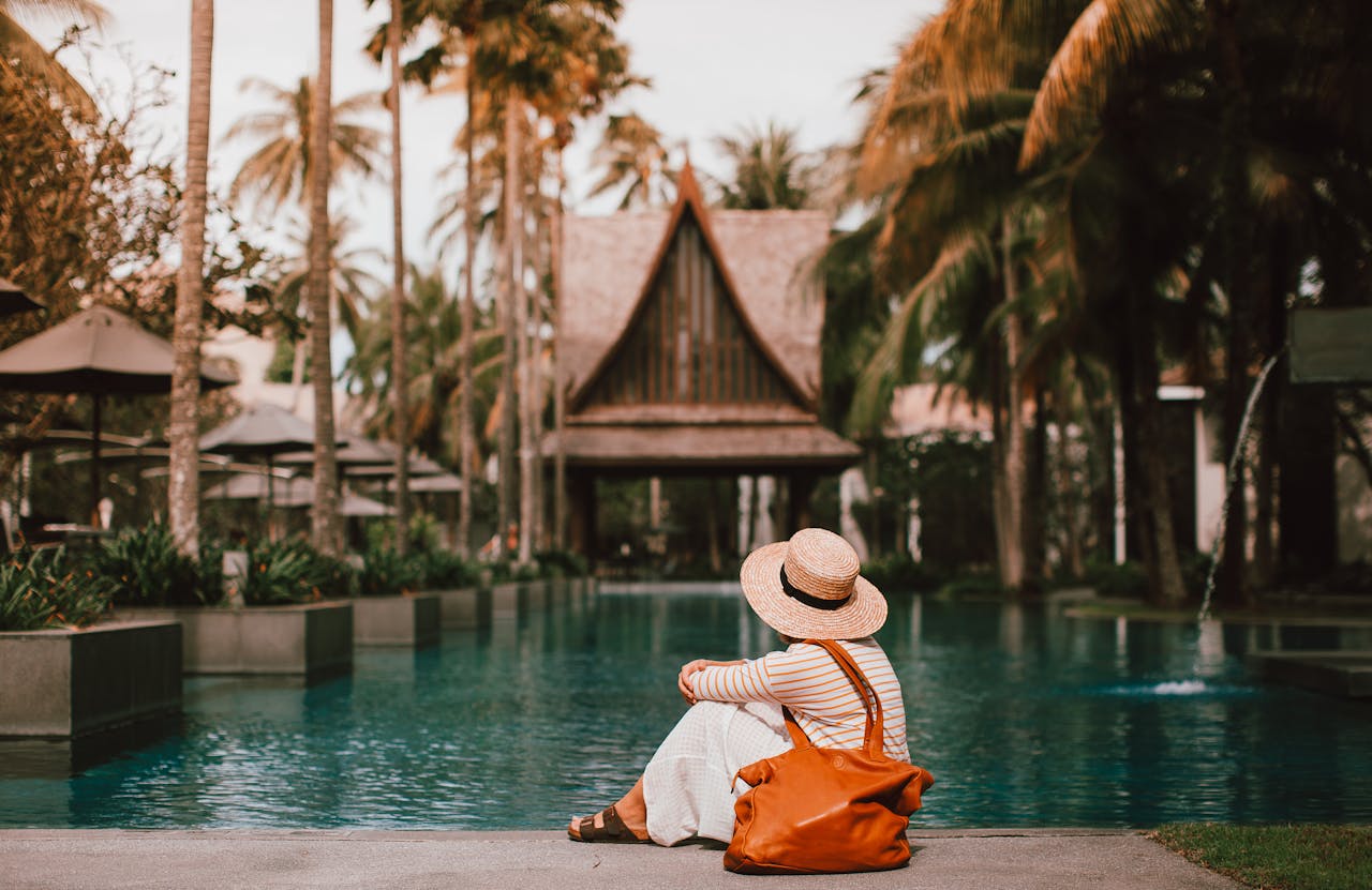 Anonymous female relaxing near calm rippling water of pond surrounded with houses and palm trees